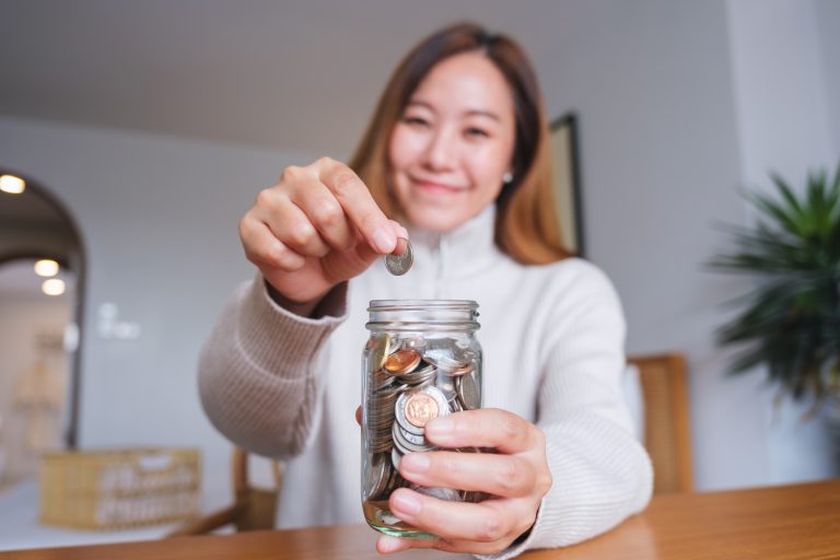 Portrait image of a woman collecting and putting coins in a glas Image description